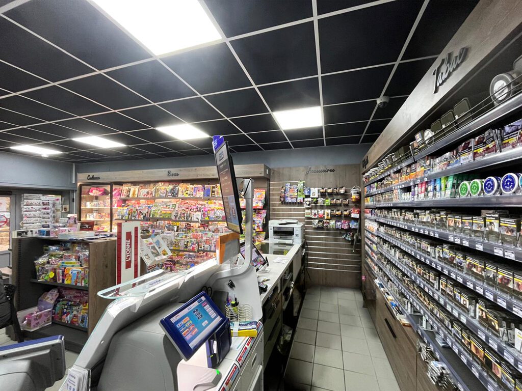 Agencement intérieur d'un tabac presse par Sudexpo : mur tabac et accessoires sur mesure, comptoir caisse, zones presse et cadeaux en fond de magasin, plafond noir suspendu