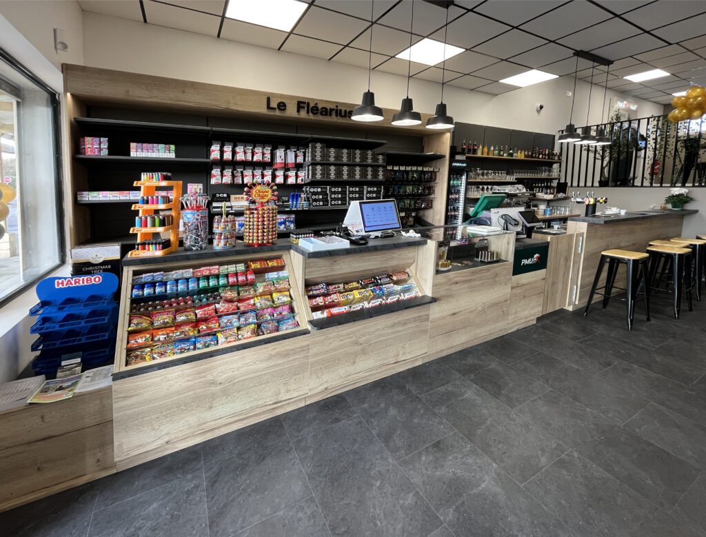 Comptoir de tabac presse “Le Fléarius” avec présentoirs de confiseries, accessoires fumeurs et espace de vente optimisé en mobilier bois et noir.