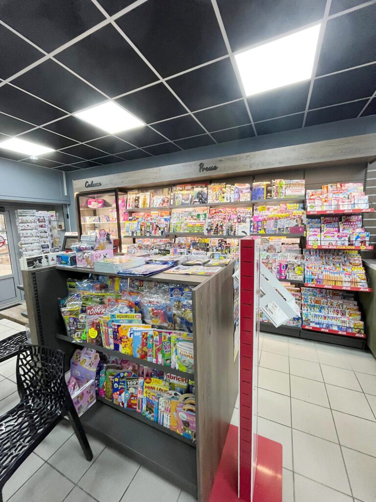 Mobilier presse et cadeaux aménagé par Sudexpo dans un tabac presse : gondoles bois, présentoirs magazines, espace jeux et zone cadeaux, plafond noir suspendu.