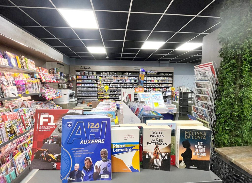 Agencement intérieur d'un tabac presse par Sudexpo : linéaire presse, espace e-liquide et tabac en fond de magasin, mur végétal décoratif et plafond noir suspendu.